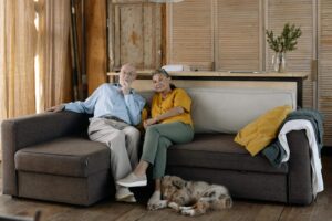 OLK9 Dog Training Blog 17 Senior couple sitting together on a modern sofa in a cozy living room with their puppy lying on the wooden floor at their feet.